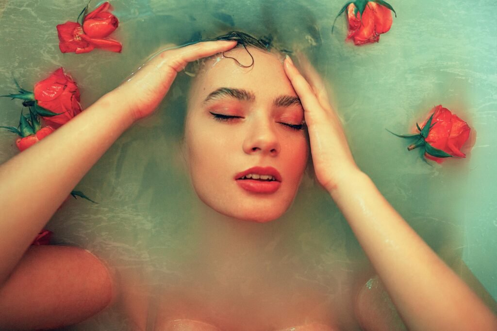 Serene woman in milky bath surrounded by red roses, eyes closed in relaxation.